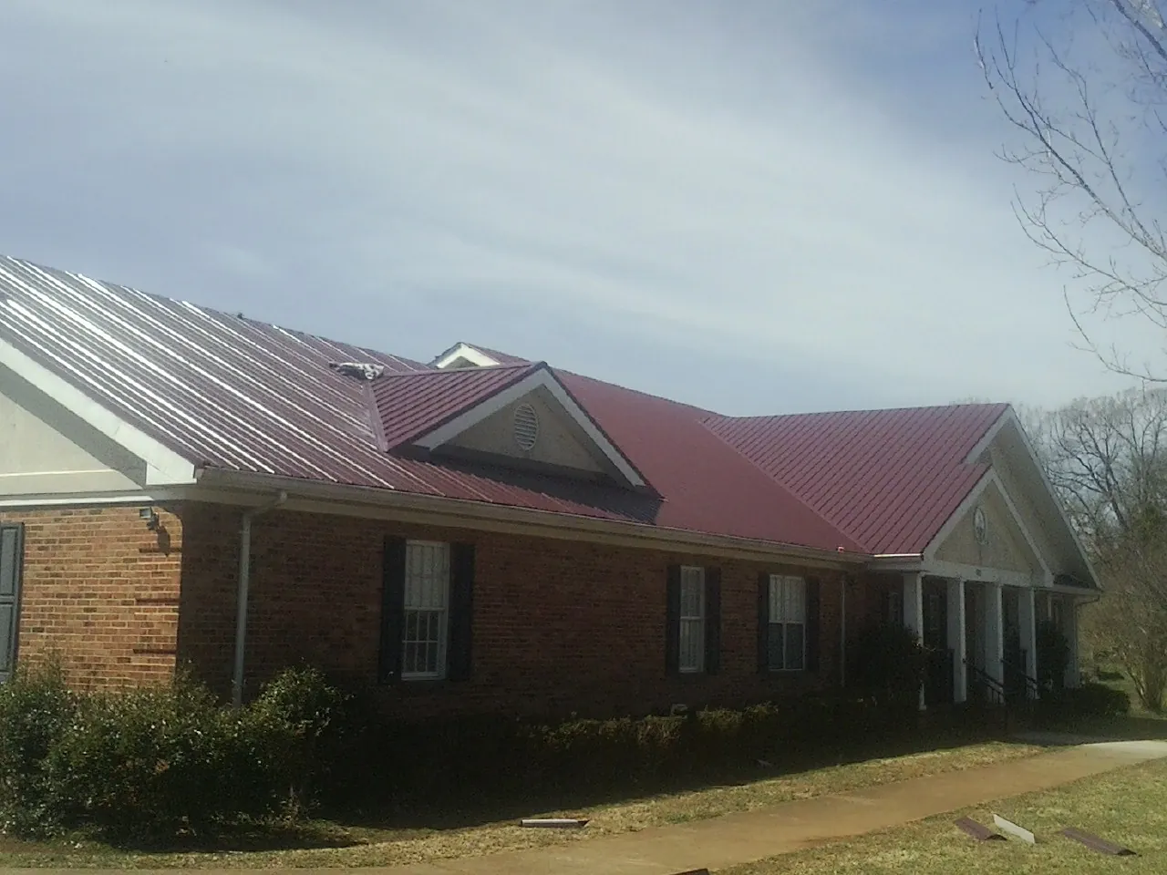 Red metal roof with gabled entries on a long brick building, from a Hail Damage Roof Repair job in Rochester